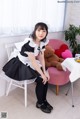 A woman in a maid outfit sitting on a chair.