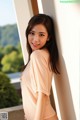 A woman in a pink top leaning against a wall.