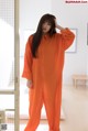 A woman in an orange jumpsuit standing in a room.