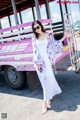 A woman in a white dress standing in front of a pink bus.