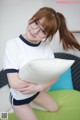 A young woman wearing glasses sitting on a couch holding a pillow.