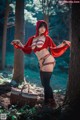 A woman dressed as a red riding hood in the woods.