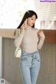 a woman in a beige turtle neck top and jeans talking on a cell phone