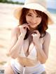 A woman in a white bikini and a straw hat on the beach.