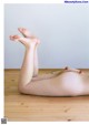 A naked woman laying on a wooden floor with a flower in her hand.