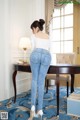 A woman in a white top and blue jeans standing in front of a desk.