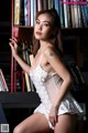 A woman in a white lingerie posing in front of a bookshelf.