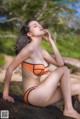 A woman in an orange bikini sitting on a rock.